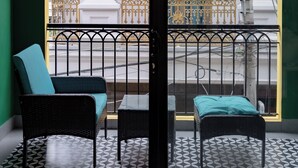 A balcony with two wicker chairs and a small table, overlooking a street with a white building and a fountain. - NHA TRONG NGO 2 (Da Nang)