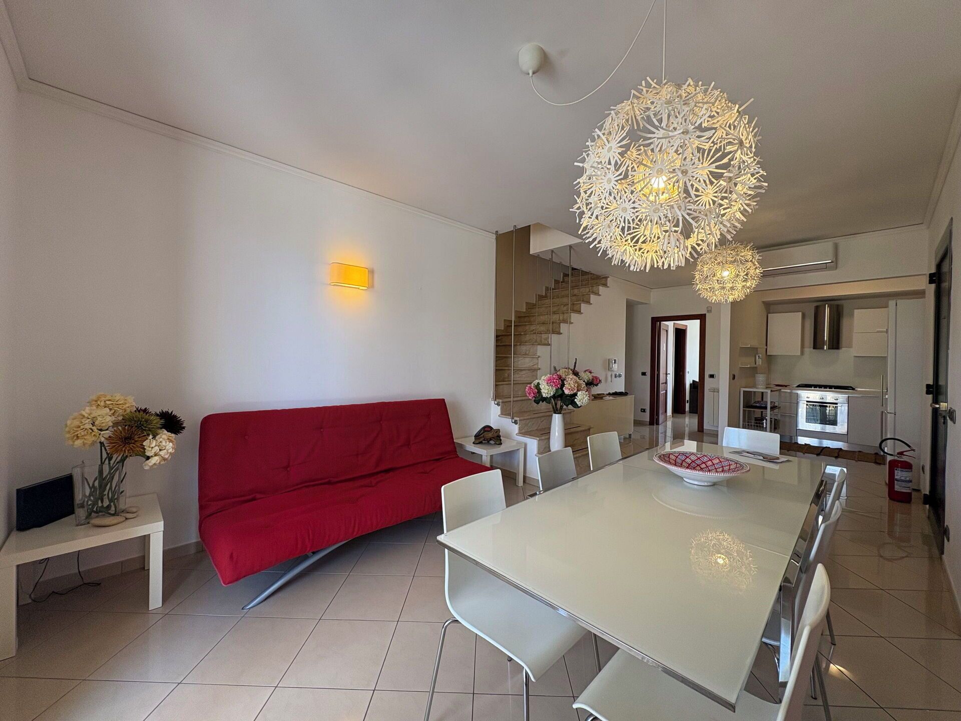 A modern living room with a red sofa, a dining table with chairs, and a kitchen area with a stove and oven.