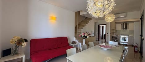 A modern living room with a red sofa, a dining table with chairs, and a kitchen area with a stove and oven.