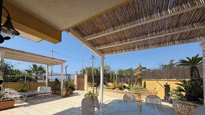 En udendørs terrasse med et glasbord og metalstole, omgivet af plantekasser og et træhegn.