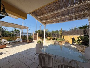 Eine Terrasse im Freien mit einem Glastisch und Metallstühlen, umgeben von Blumentöpfen und einem Holzzaun.
