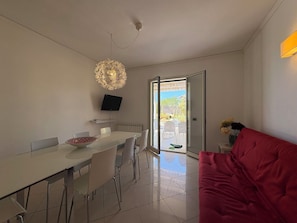 Ein moderner Essbereich mit einem weißen Tisch und Stühlen, einer dekorativen Deckenleuchte und einem an der Wand montierten Fernseher.