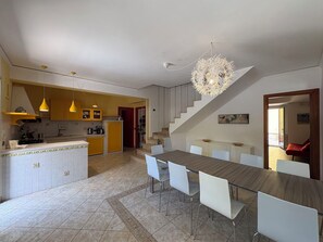 Eine moderne Küche mit gelben Schränken, ein Essbereich mit einem Holztisch und weißen Stühlen sowie eine Treppe, die zu einer oberen Ebene führt.
