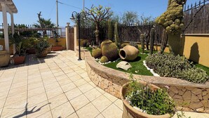 En anlagt have med forskellige kaktusser og planter, en fliseterrasse og et hegn.