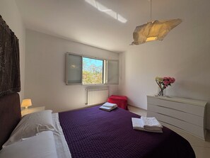 Um quarto com cama, cômoda, janela e radiador.