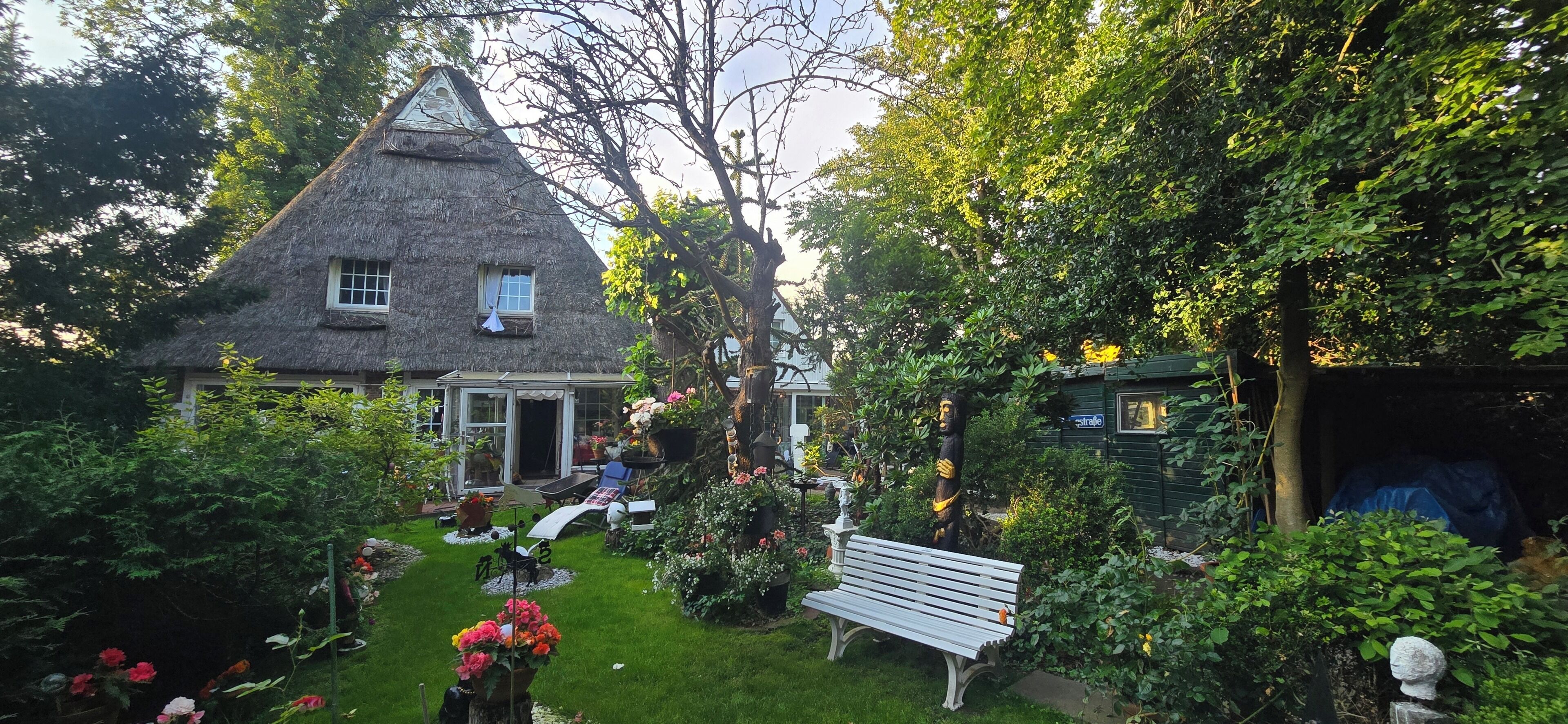 Een rieten huis met een tuin, een bankje en een kleine schuur.