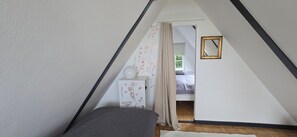 A bedroom with a sloped ceiling, a bed, a bedside table, a nightstand, a mirror, and a window with curtains. - OASE AM DEICH (Krummendeich)
