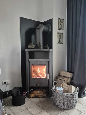 A corner room with a black wood-burning stove, a basket of firewood, and a power outlet. - OASE AM DEICH (Krummendeich)