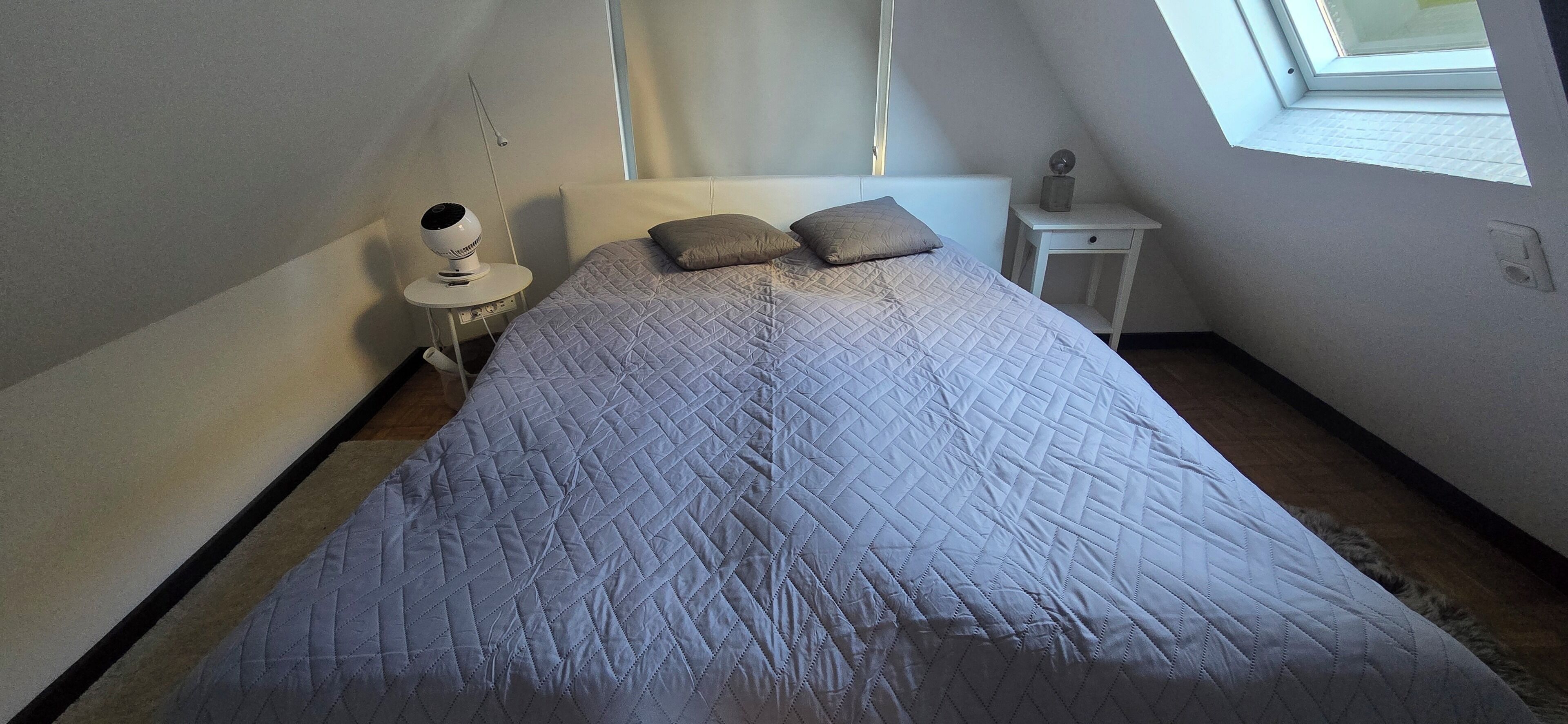 A bedroom with a bed, a nightstand, a lamp, and a window.