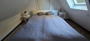 Een slaapkamer met een bed, nachtkastje, lamp en raam.
