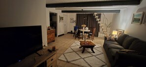 Un salon comprenant un téléviseur, un canapé, une table basse et un coin repas avec des chaises et une table.
