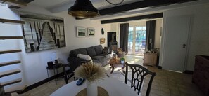 A living room with a sofa, a coffee table, and a dining table with chairs. There is a large painting on the wall and a window with curtains. - OASE AM DEICH (Krummendeich)