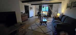 Een woonkamer met een televisie, een bank, een salontafel en een eethoek met stoelen en een tafel.