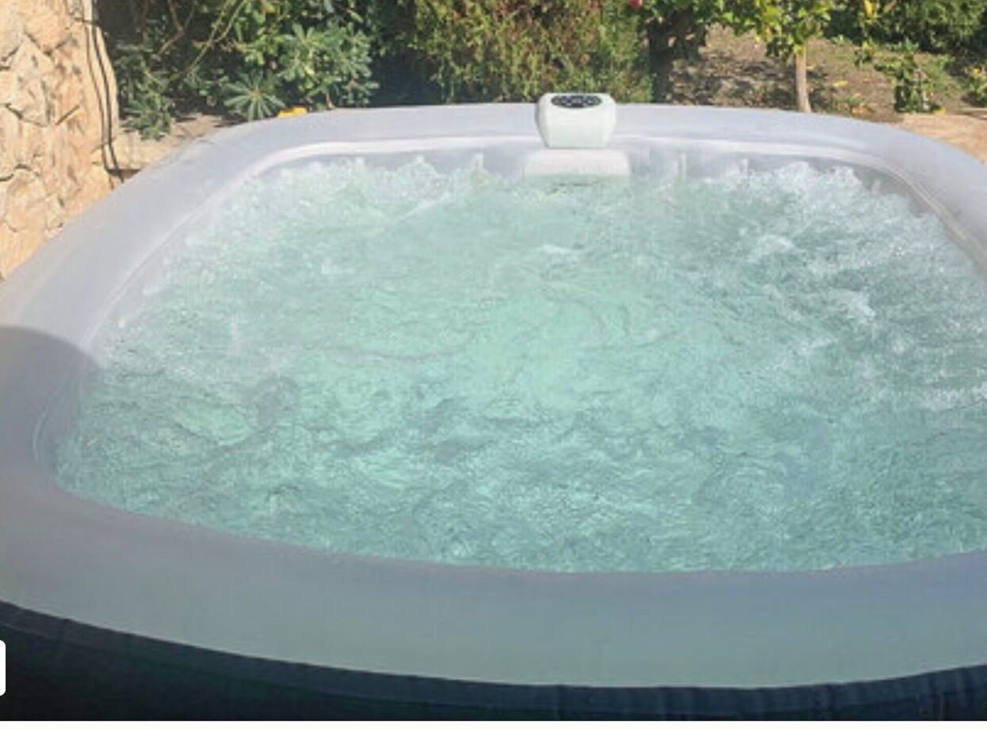 Ein Whirlpool, gefüllt mit Wasser, umgeben von einer Steinmauer und Pflanzen.