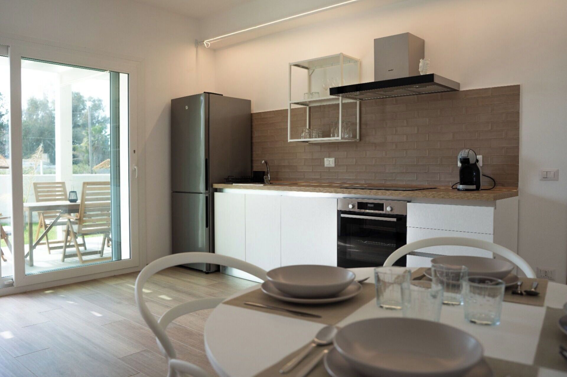 Een moderne keuken met een koelkast, oven en koffiezetapparaat. Er is een eethoek met een tafel en stoelen.