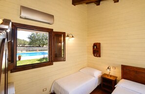 Ein Zimmer mit zwei Betten, einem Fenster mit Blick auf einen Swimmingpool, einem Wandheizkörper und einem Regal mit Flaschen.
