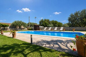 Ein Swimmingpool mit Liegestühlen, einer Steinmauer und einem kleinen Gebäude.