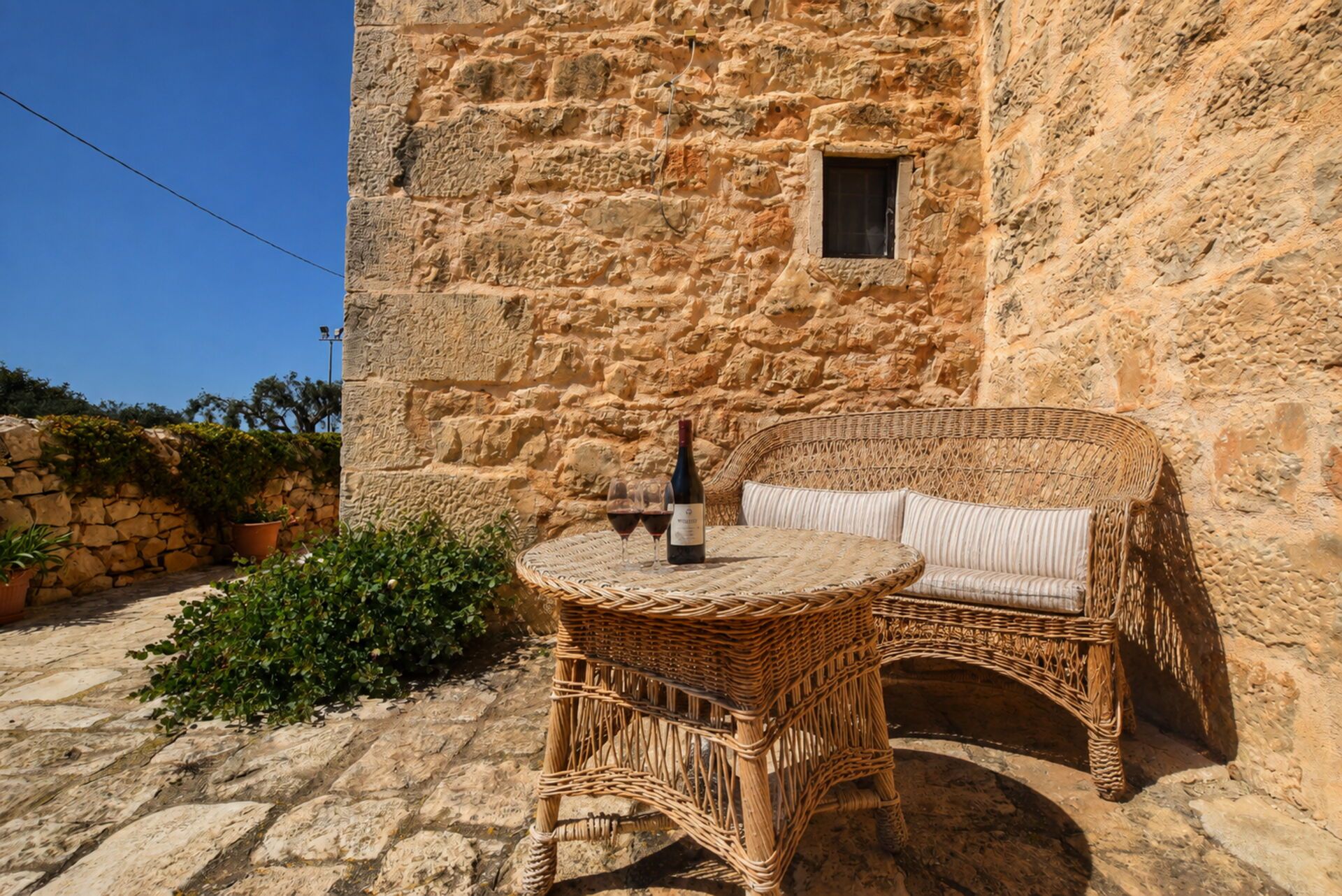 Un edificio de piedra con una silla y mesa de mimbre, una botella de vino y dos copas.
