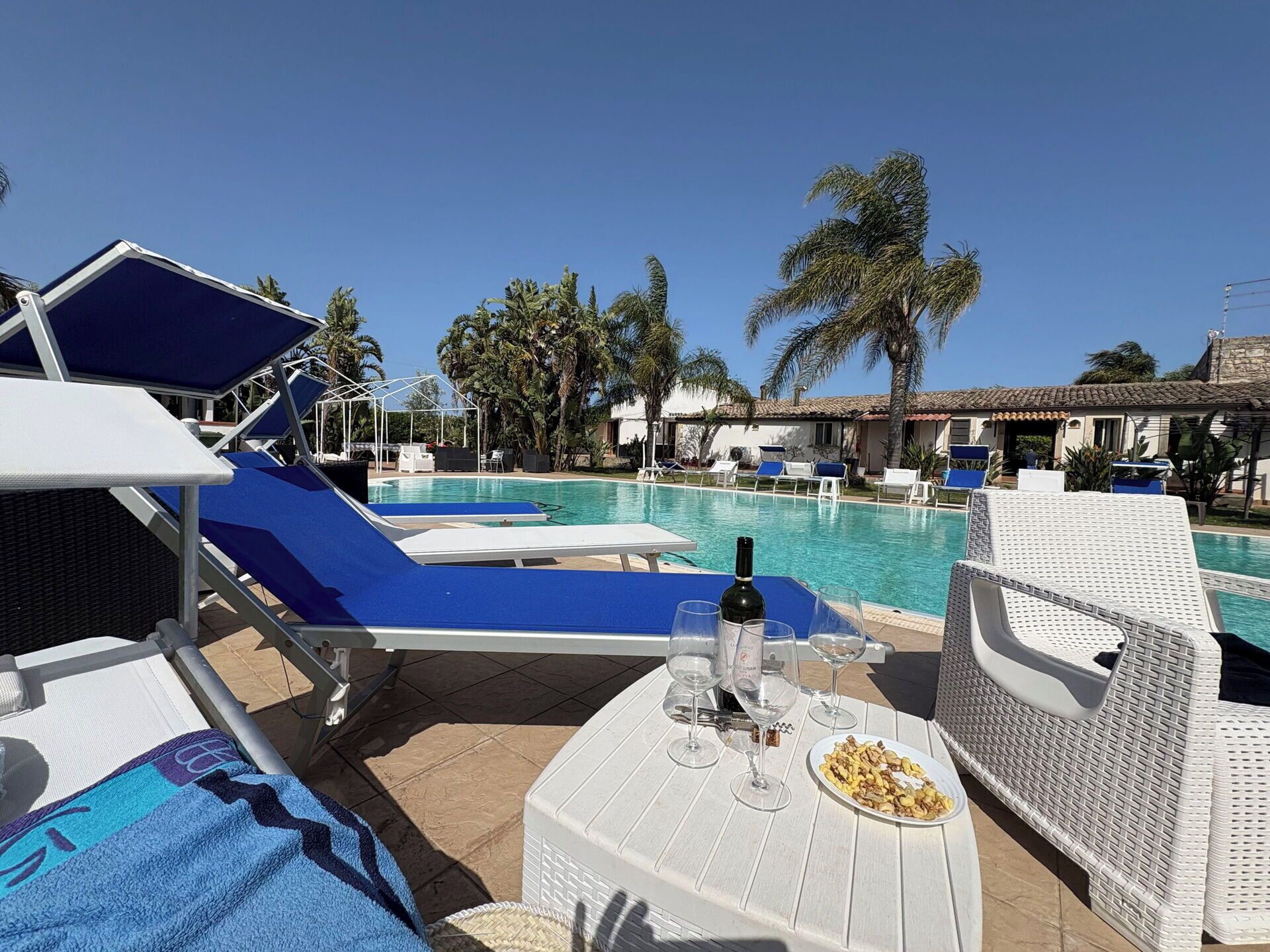 A poolside area with lounge chairs, a table with a bottle and glasses, and a view of the pool and palm trees.