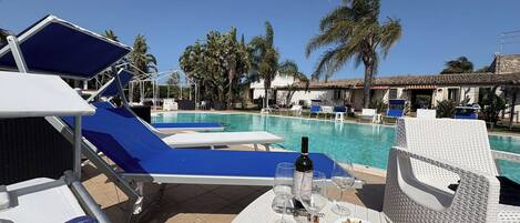 A poolside area with lounge chairs, a table with a bottle and glasses, and a view of the pool and palm trees.