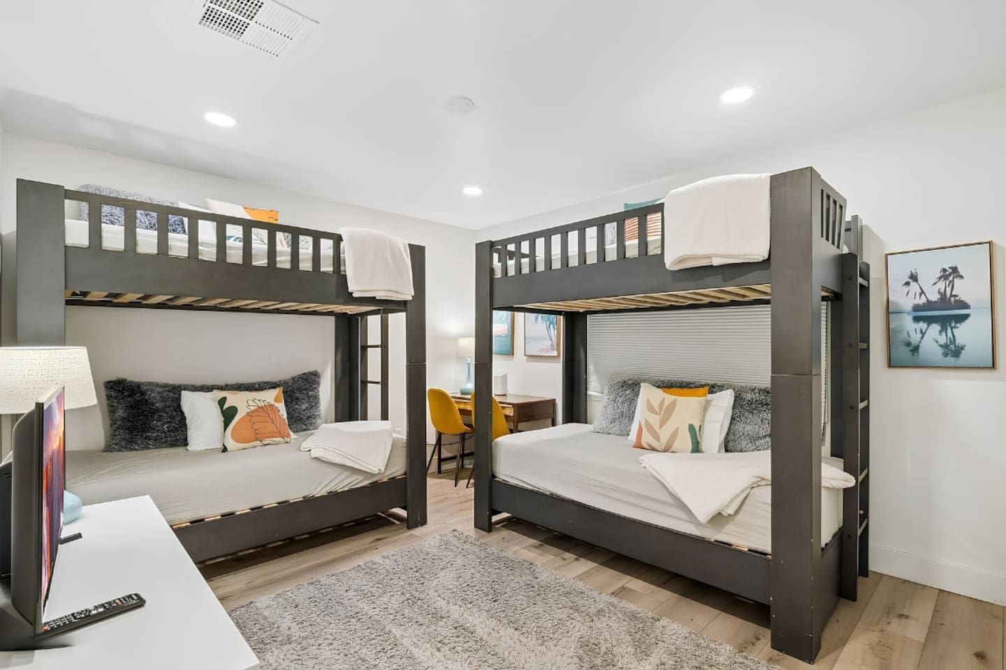 A room with two bunk beds, a desk, a chair, and a television.