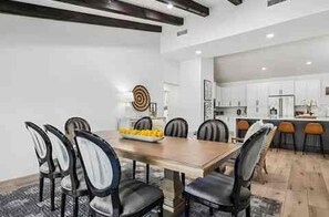 A modern dining area with a wooden table and black chairs, a kitchen in the background, and a decorative wall piece. - The Rally House-Premium 4 bed, priv pool, pickleball, 5 hole golf — mins to TPC (Scottsdale)