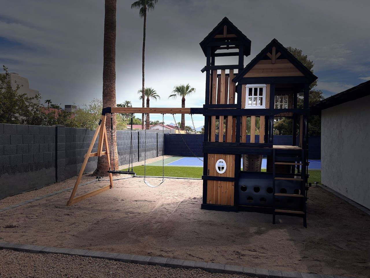 A children's play area with a swing set and a multi-level wooden playhouse.