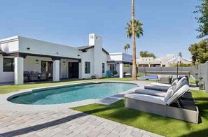 Ein modernes Haus mit Swimmingpool, überdachter Terrasse und gepflegtem Rasen.