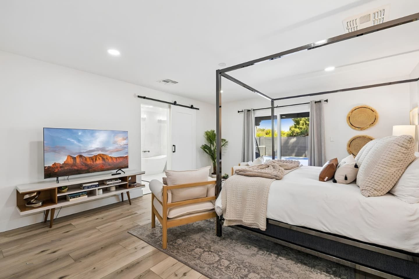 Une chambre moderne avec un lit à baldaquin, un téléviseur à écran plat, une chaise en bois et une grande fenêtre donnant sur un paysage verdoyant.