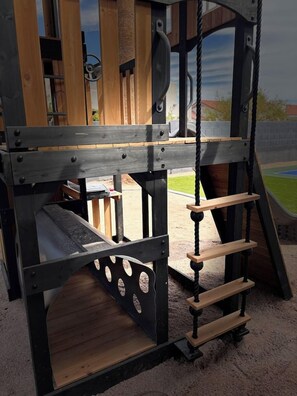 A playground structure with a wooden slide, a rope swing, and a climbing ladder. - Scottsdale Pool, Spa, Theater, Arcade & Golf (Scottsdale)