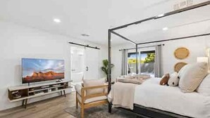Une chambre à coucher moderne avec un lit à baldaquin, un téléviseur posé sur un meuble et une vue sur l’extérieur par une fenêtre.