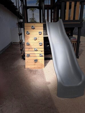 A playground with a wooden climbing wall and a grey slide. - Scottsdale Pool, Spa, Theater, Arcade & Golf (Scottsdale)