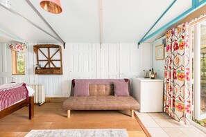 A cozy room with a sofa, a bed, a radiator, a window, and a small kitchenette. - Stunning Glamping Retreat in the Woods - Pass the Keys (Moreton-in-Marsh)