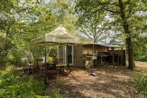 A rustic cabin with a covered patio, wooden furniture, and a hanging chair. - Stunning Glamping Retreat in the Woods - Pass the Keys (Moreton-in-Marsh)