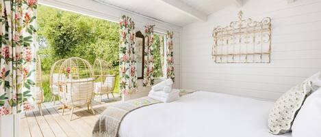 A bedroom with a bed, a hanging light fixture, a window with curtains, and a view of greenery outside.