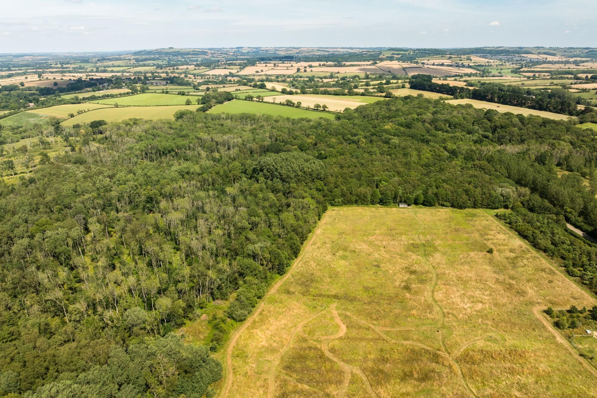 Oversigtsbillede af et landligt landskab med marker, skove og en klar himmel.
