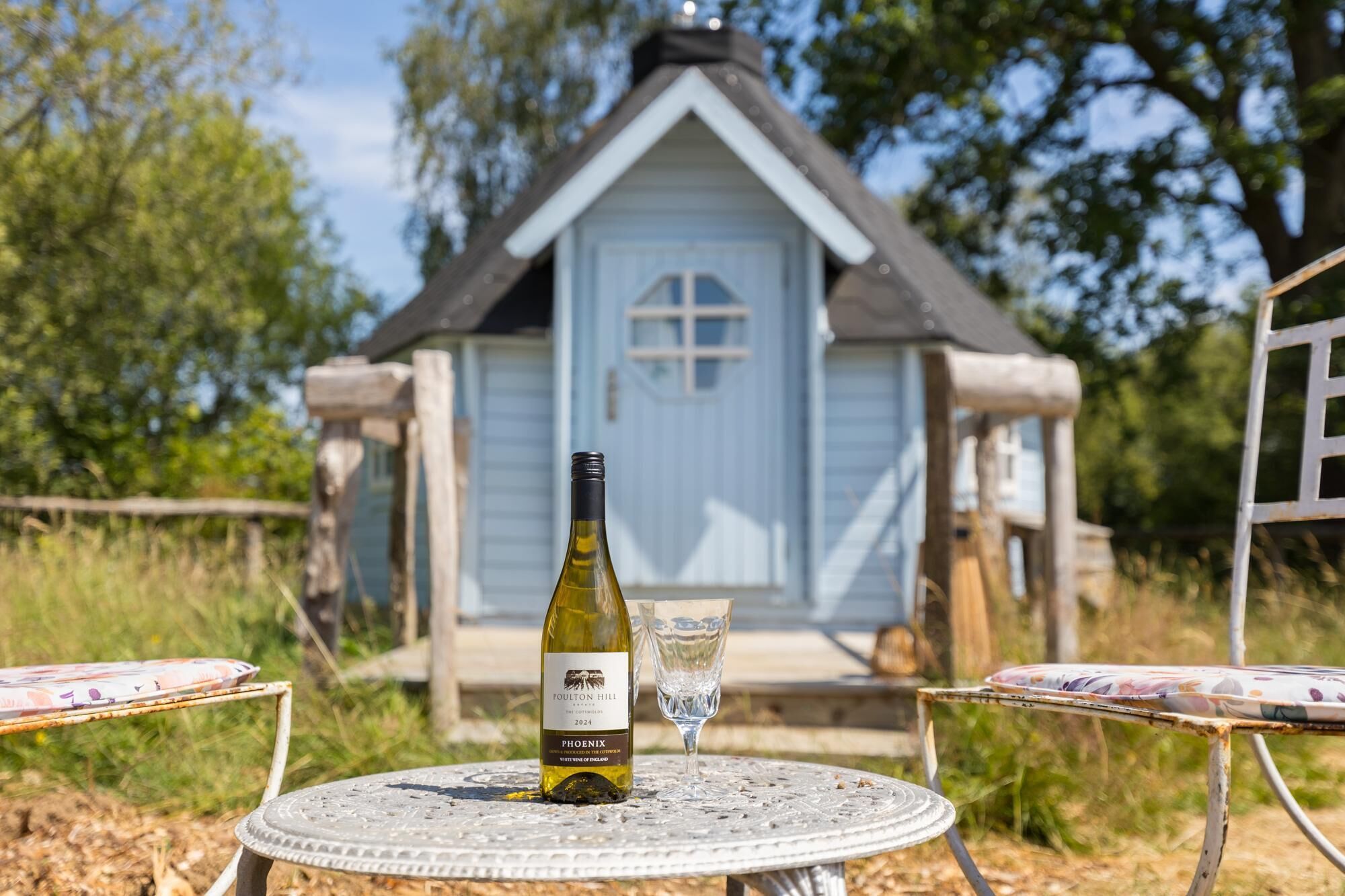 A bottle of wine and a glass on a table with a view of a small house in the background.