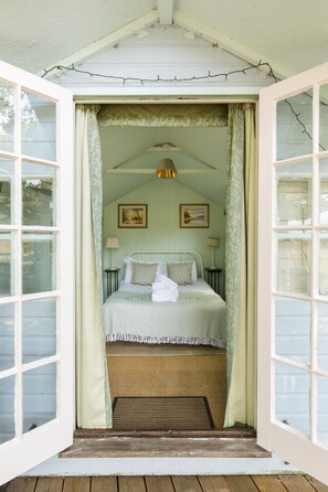 Een kamer met een bed, een raam, een lamp en een plafondventilator.