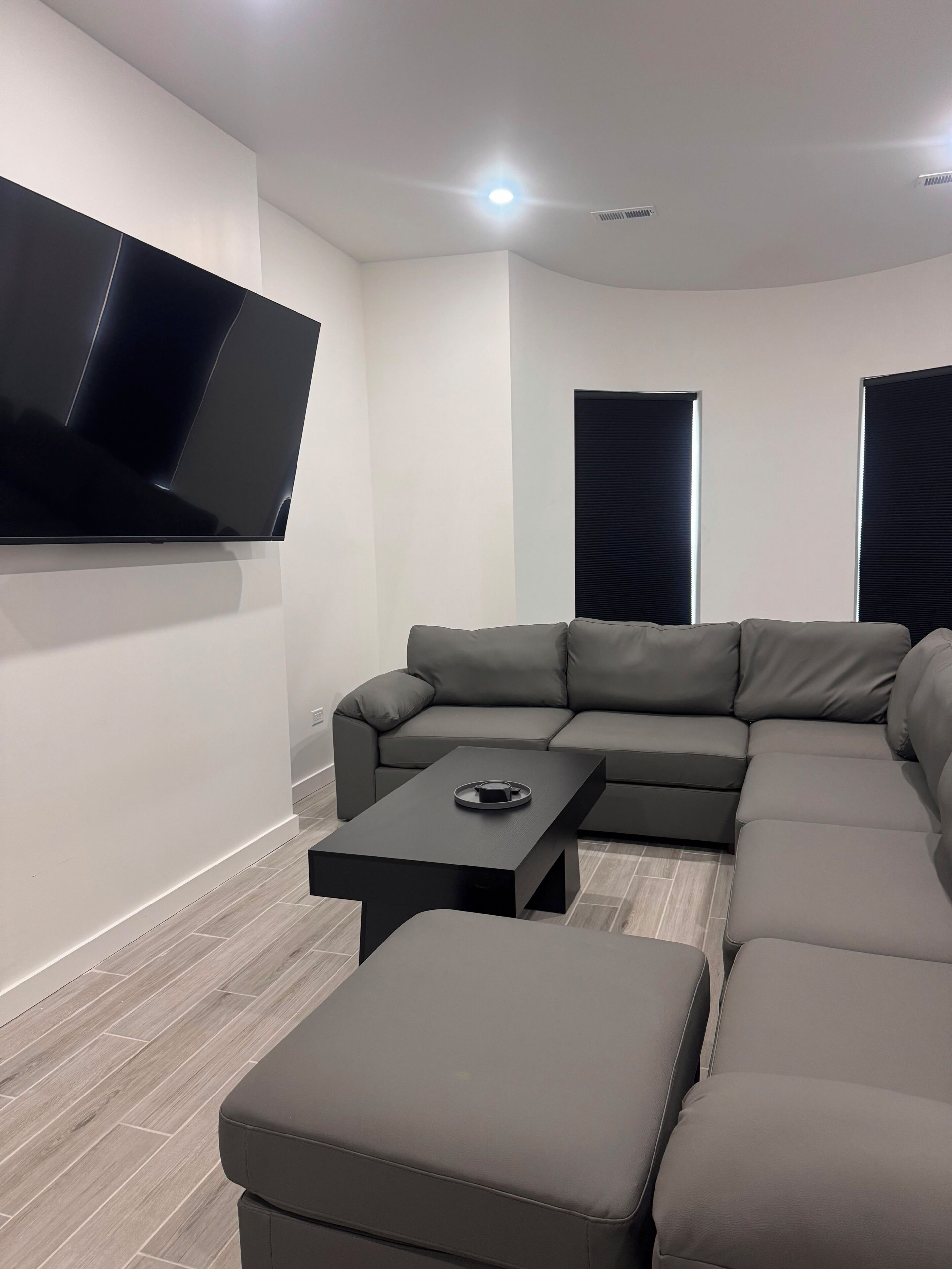 A modern living room with a sectional sofa, a flat-screen TV mounted on the wall, and a coffee table.