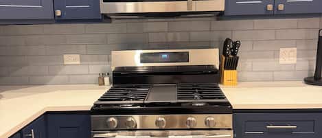 A kitchen with dark blue cabinets, a stainless steel microwave, a black Samsung oven, and a countertop with kitchen utensils.