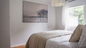Une chambre à coucher avec un lit, une fenêtre avec des rideaux, un tableau au mur et un luminaire suspendu.