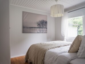 Une chambre à coucher avec un lit, une fenêtre avec des rideaux, un tableau au mur et un luminaire suspendu.