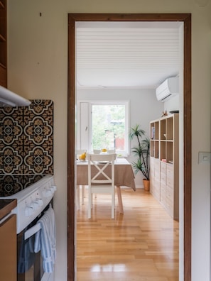 A hallway leading to a dining area with a table set for two, a potted plant, and a wooden cabinet.