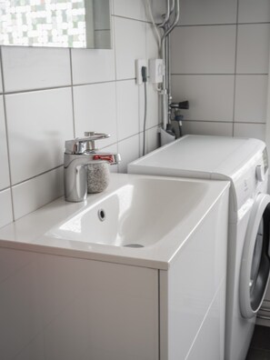 Une salle de bain moderne avec un lavabo blanc, un lave-linge et un miroir.