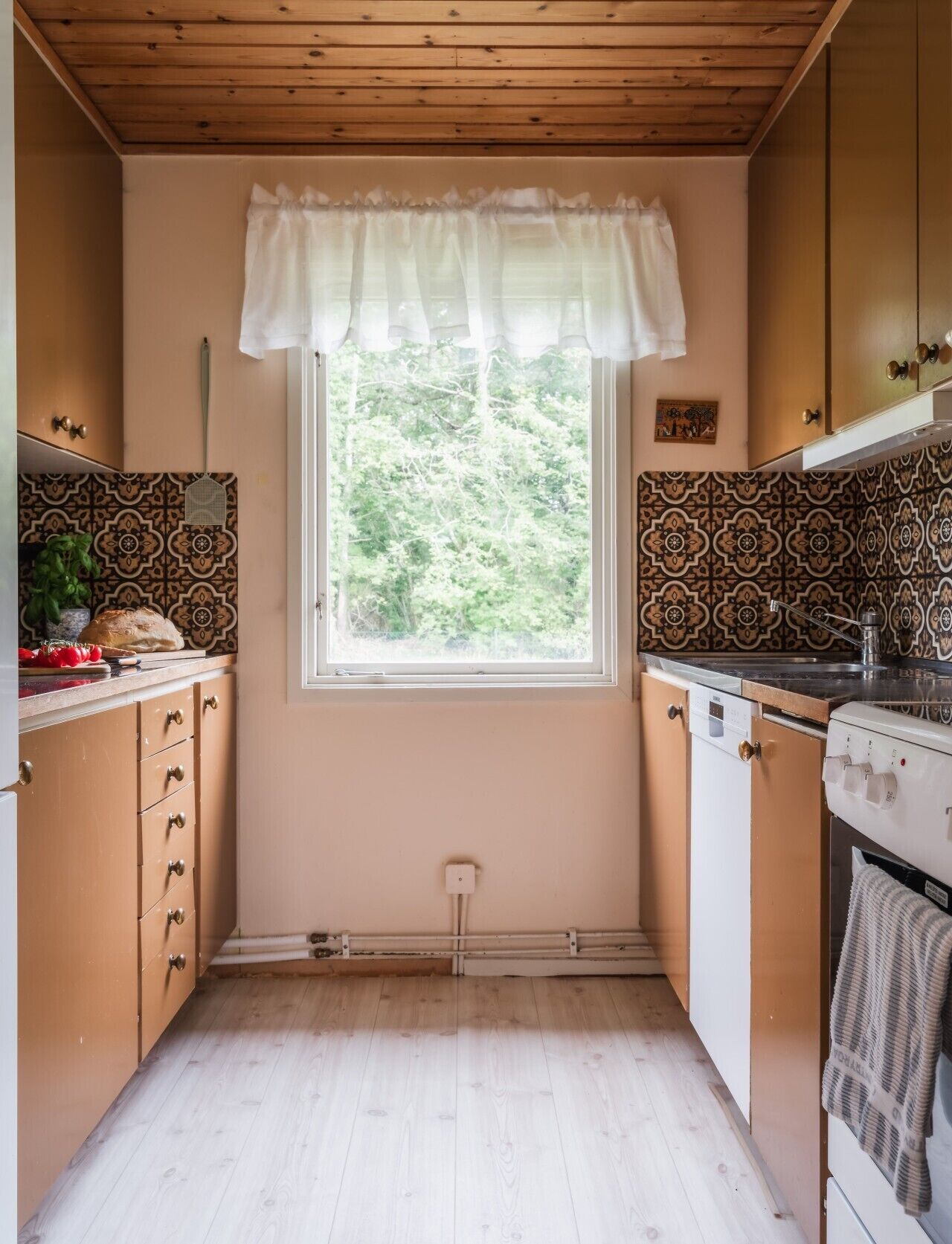 A kitchen with wooden cabinets, a window with a white valance, patterned backsplash, and a stove.