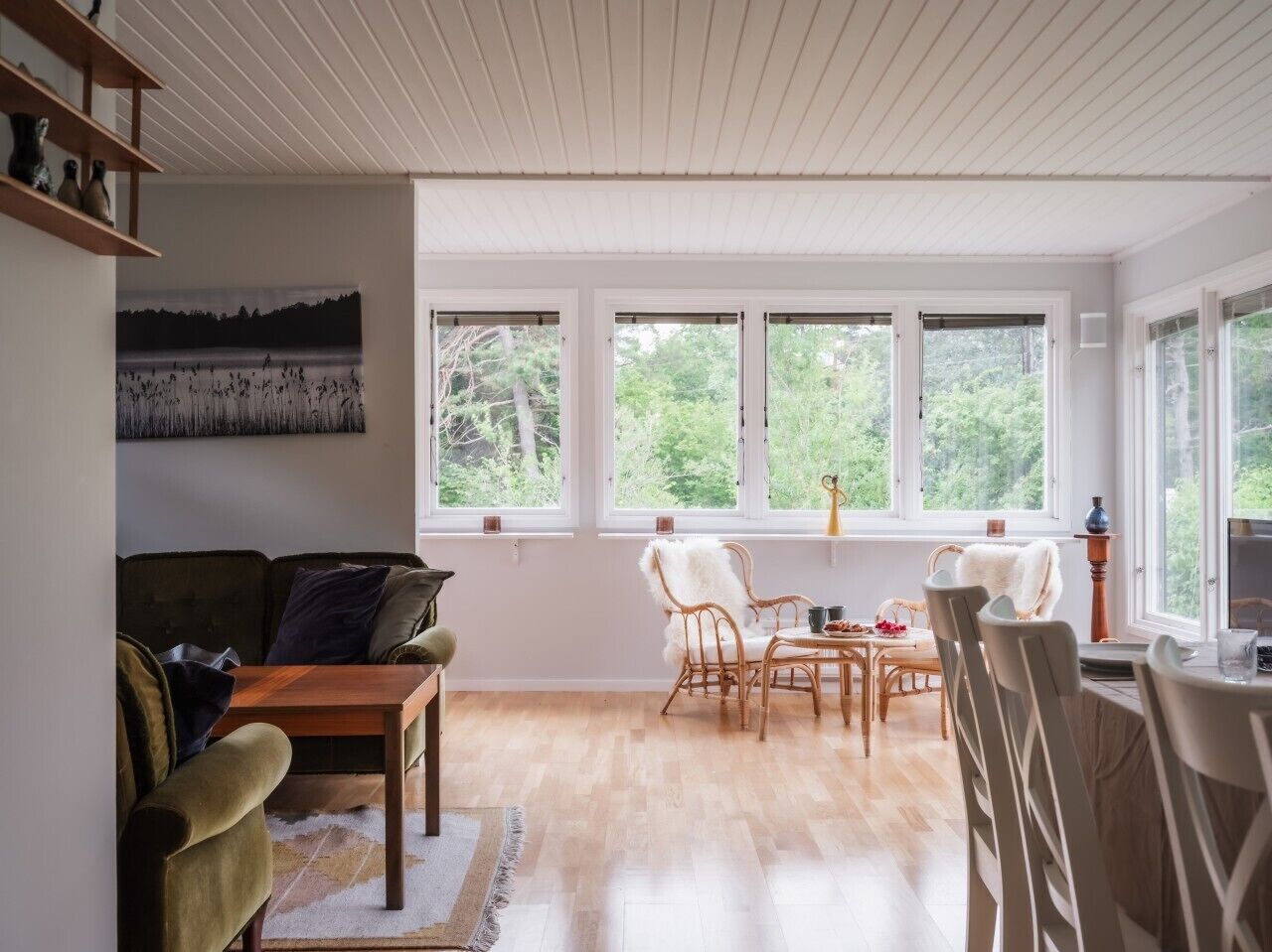 Un amplio salón con piso de madera, un sofá, una mesa de comedor con sillas y grandes ventanales con vista a la vegetación.