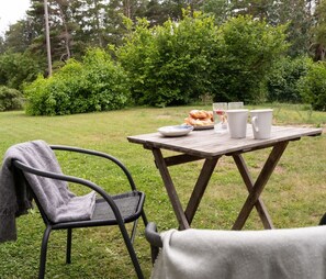 Un coin pique-nique aménagé avec une table, une chaise et une couverture, dans un espace extérieur herbeux.