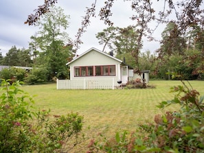 A single-story house with a white exterior and a porch, surrounded by a grassy yard and trees.
