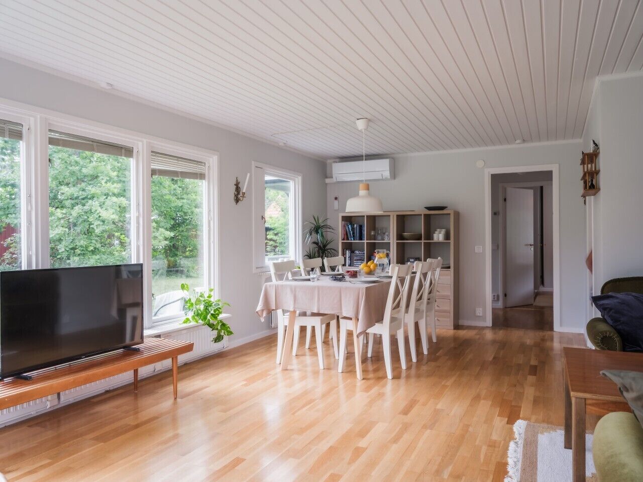 En rummelig opholdsstue med spisebord, stole, fjernsyn og en reol.