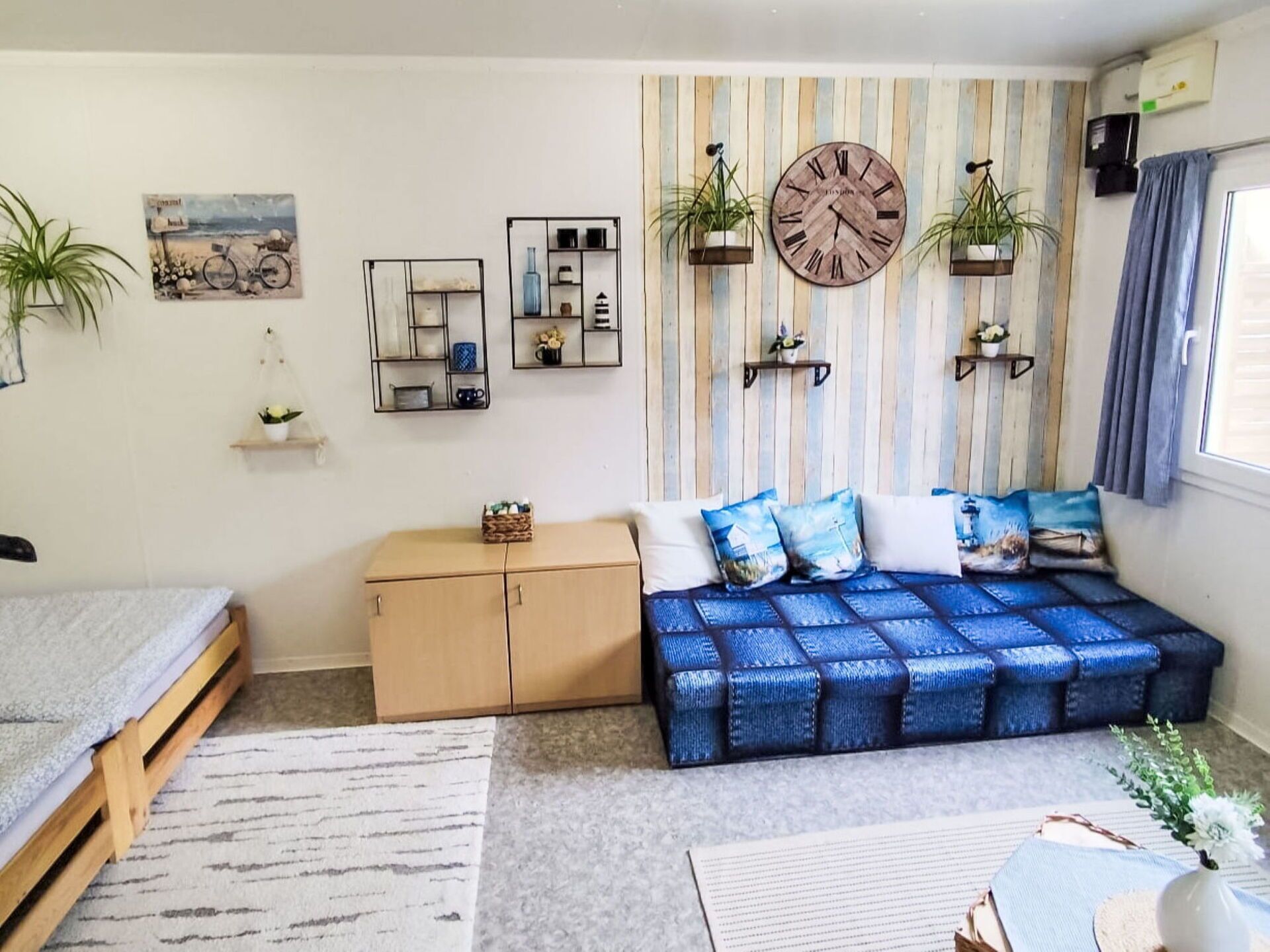 Un dormitorio moderno con sofá cama, un armario de madera, un reloj de pared y plantas decorativas.
